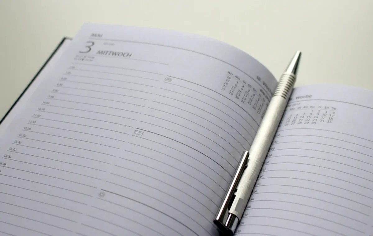 An open desk diary at a page headed with the day's number and the name of the weekday, with a pen lying across it