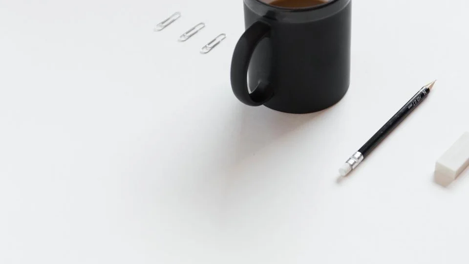 Three paper clips laid in a row on a white desk beside a black mug, a pencil and an eraser